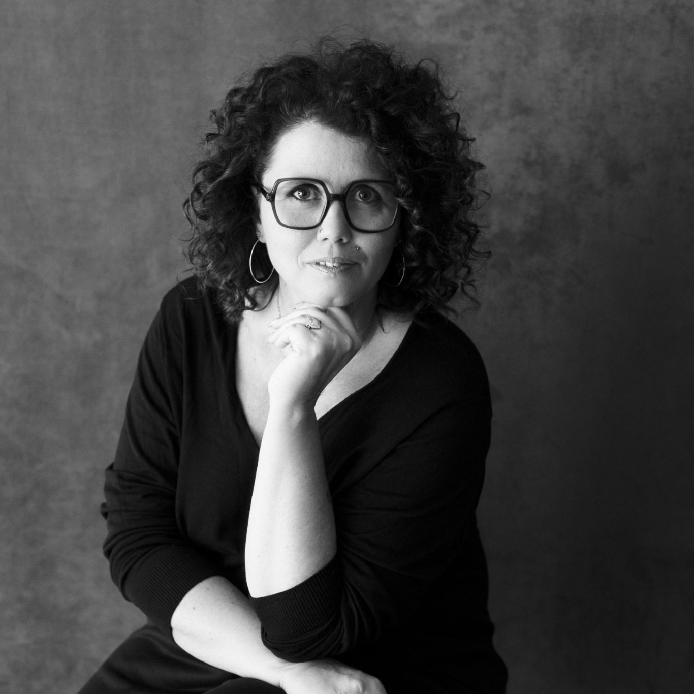 Photographe Thonon Femme aux cheveux bouclés, portant des lunettes, assise pensivement sur une chaise.